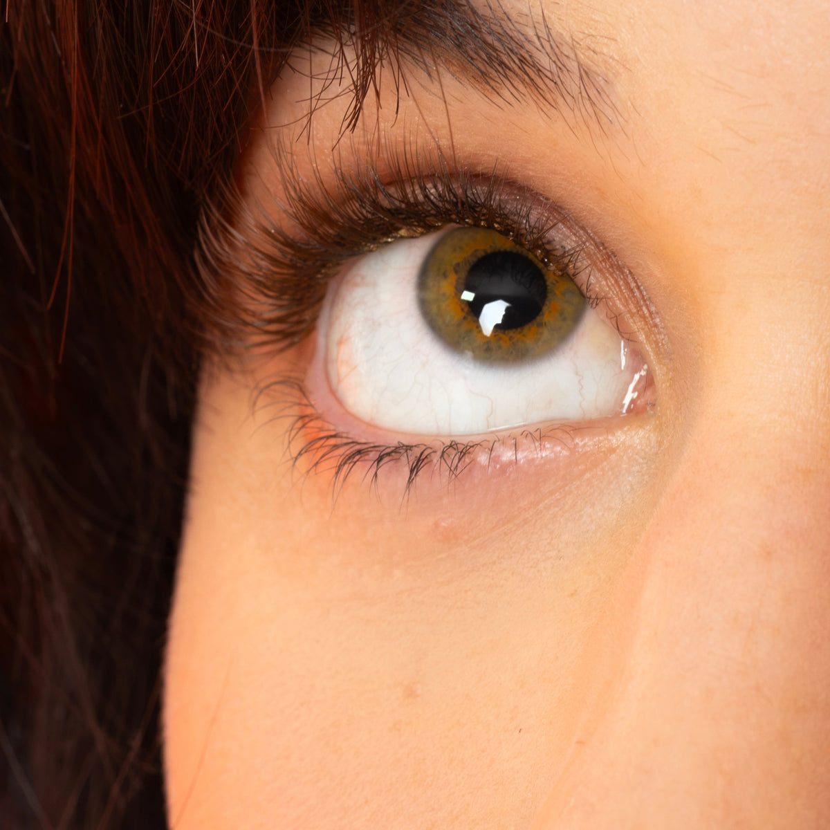 Extreme close-up of a human eye with dark hair on the left and a soft peach-pink background.